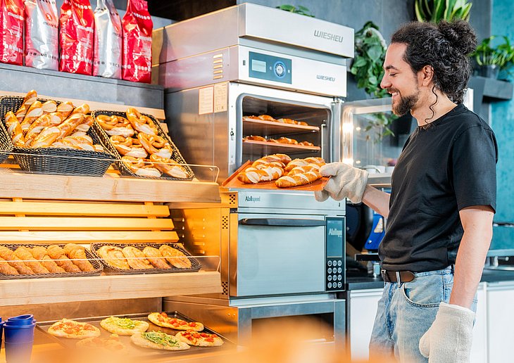 Employee removing freshly baked pastries from a Wiesheu Minimat oven