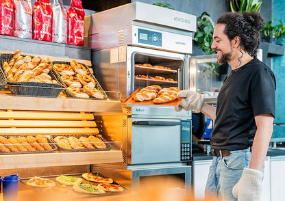 Employee removing freshly baked pastries from a Wiesheu Minimat oven
